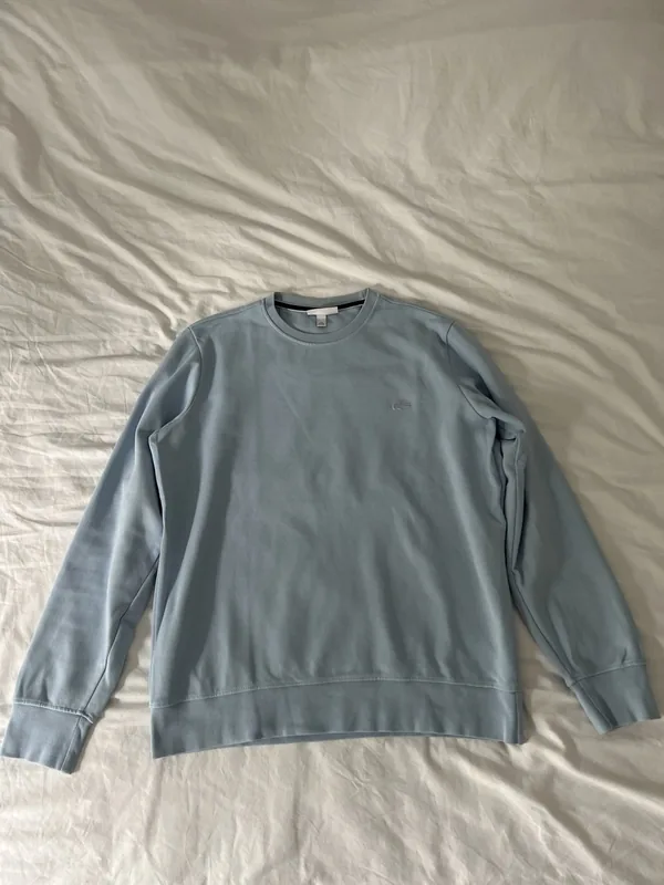 A light blue sweatshirt lying on an unmade bed, photographed with a phone.